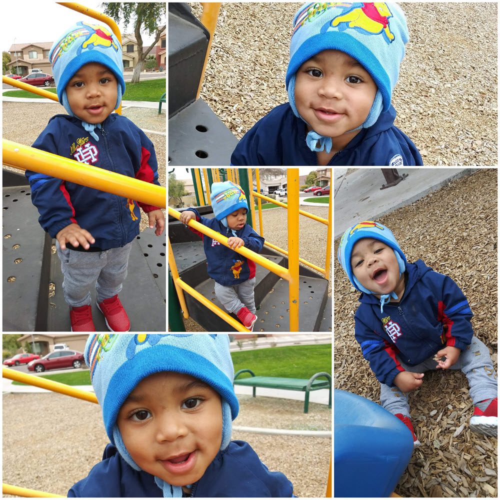 Toddler smiling and playing on playground equipment while wearing a blue winter hat, navy jacket, gray pants, and red shoes.